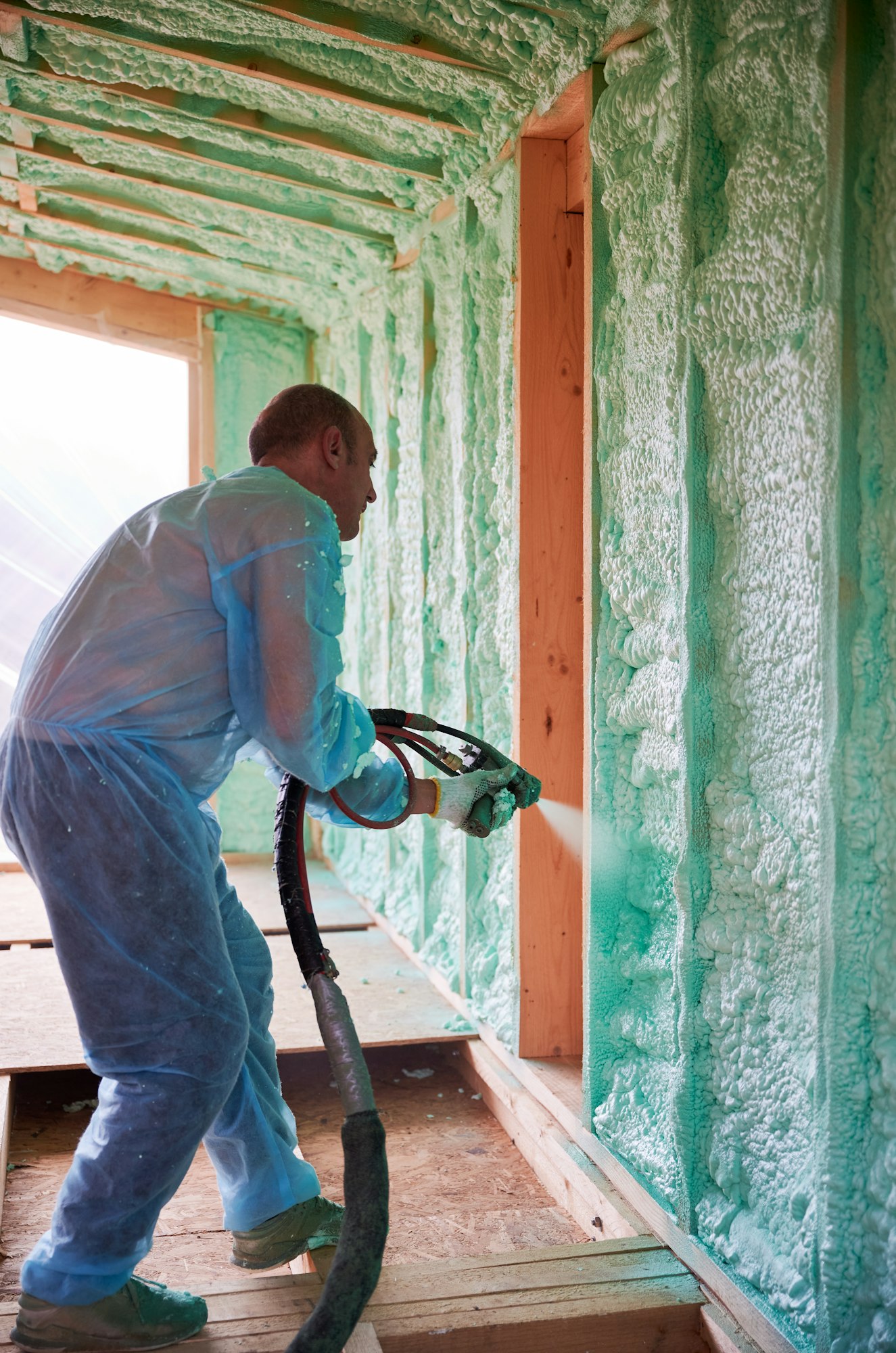 Worker spraying polyurethane foam for insulating wooden frame house.